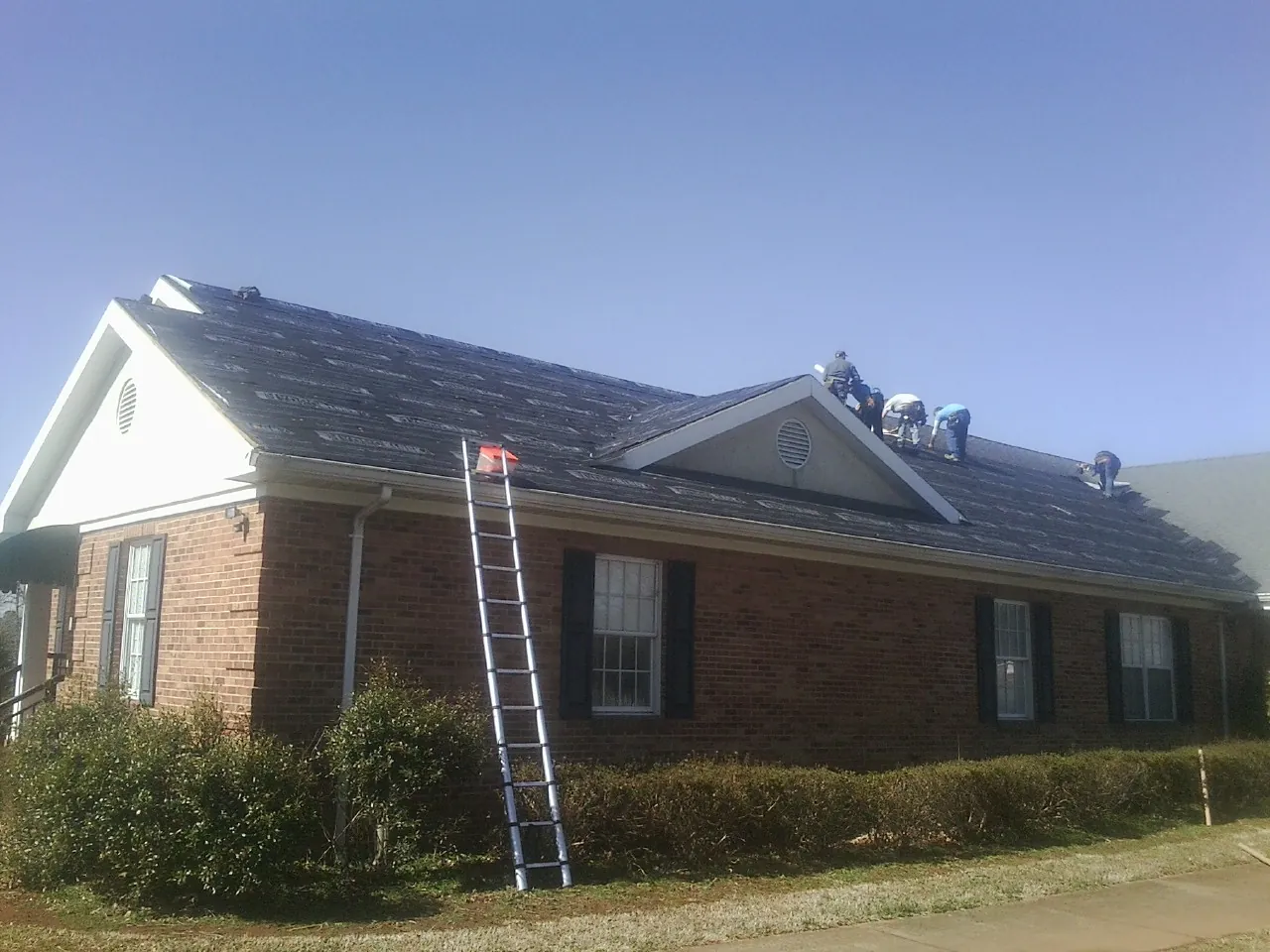 Crew tearing shingles off a brick ranch roof with a ladder set — Emergency Roof Repair work by our crew in Hughesville