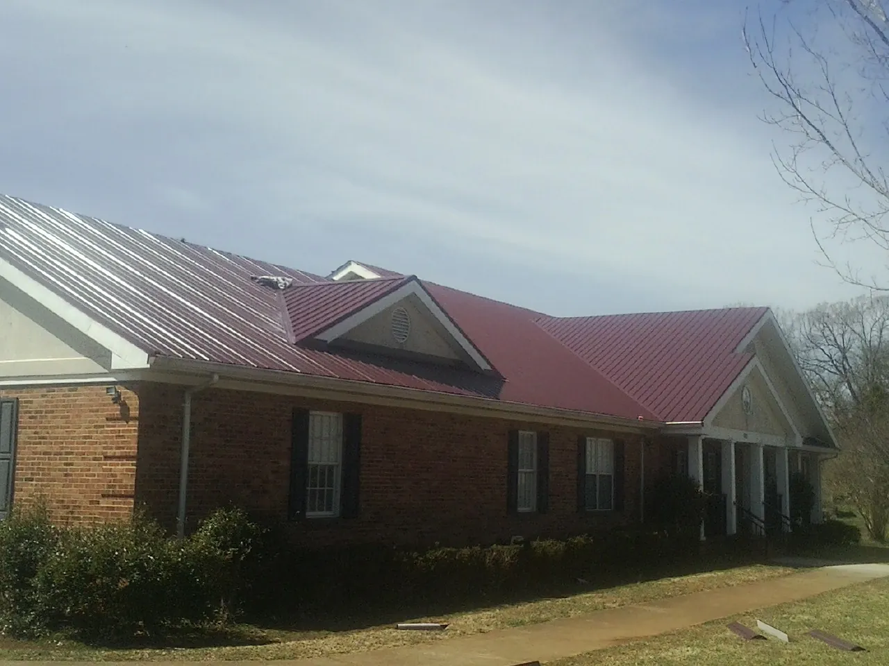 Red metal roof with gabled entries on a long brick building, from a Hail Damage Roof Repair job in Hughesville