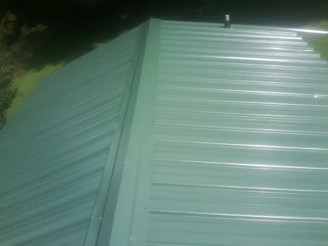 New green metal panels meeting at the ridge of a roof — Flat Roof Repair work by our crew in Hughesville
