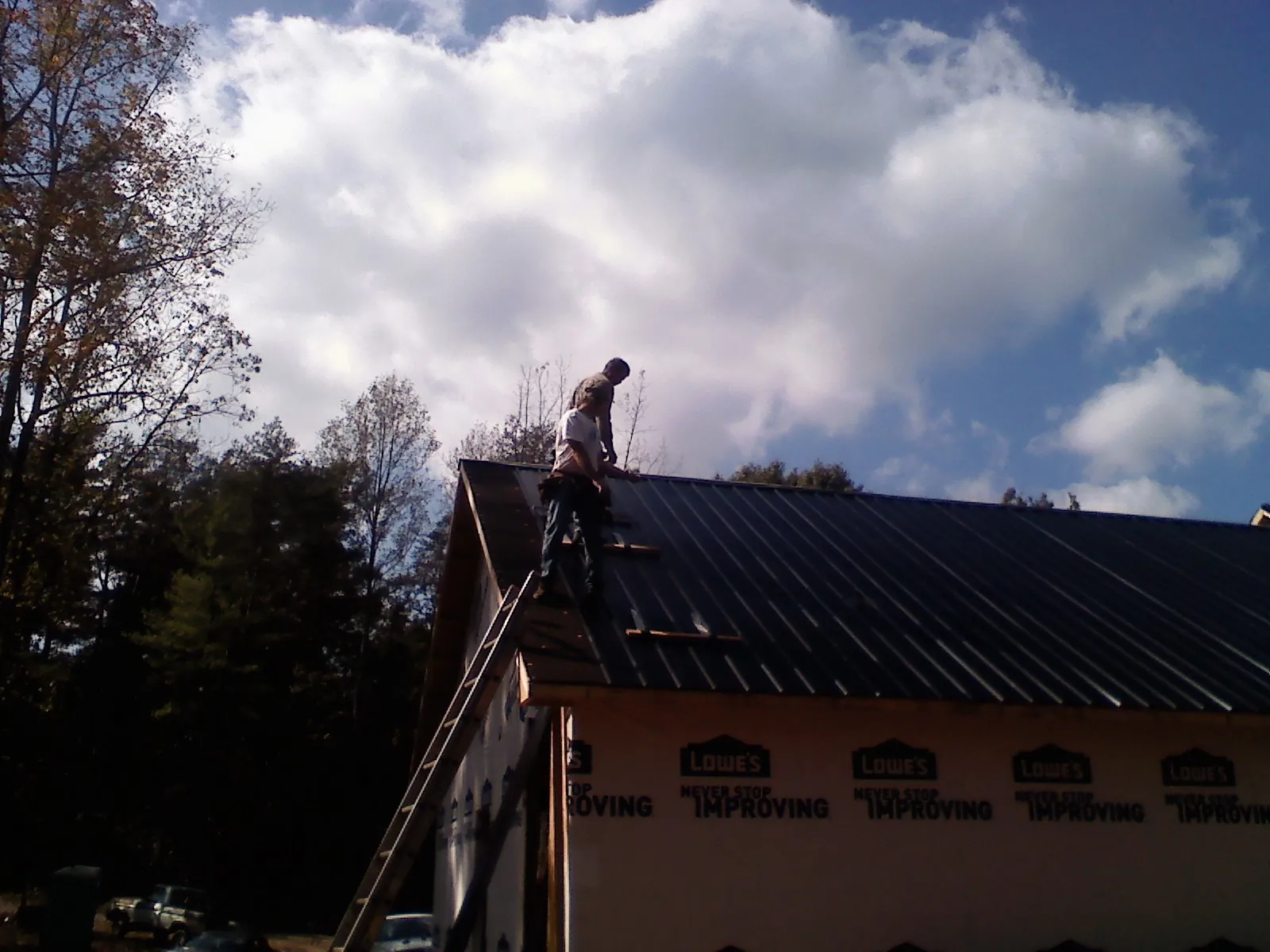 Roofer fastening dark metal panels high against a cloudy sky, from a Roof Inspection job in Hughesville