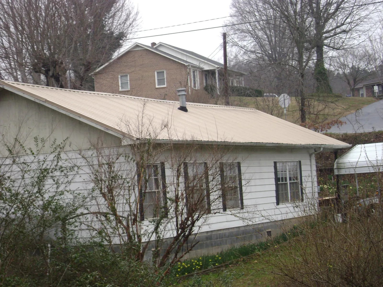 Tan metal roof on a white sided house set into a hillside — Commercial Roofing by Roofing Brothers in Hughesville